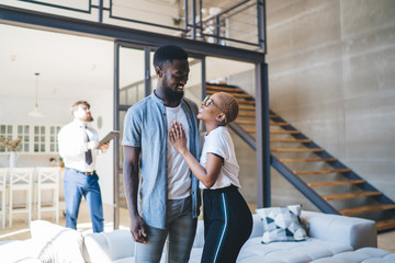 Elated ethnic couple hugging while standing at new apartment with real estate agent