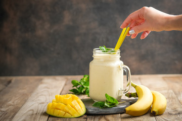 .Female hands with mango and banana smoothie on a rustic background. Healthy food, detox diet.