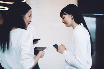 Female coworkers talking while using gadgets