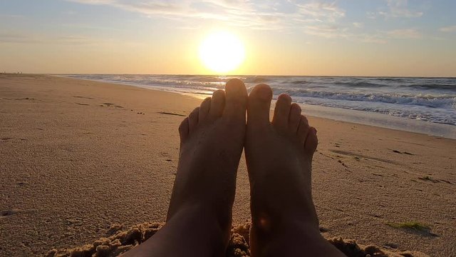 The girl is sitting near sea and waves roll on her feet on sandy beach