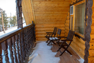 Balcony of a modern wooden chalet with three chairs covered by fresh snow. Tourism and winter vacation concept. Winter wooden house in a forest, village cottage 