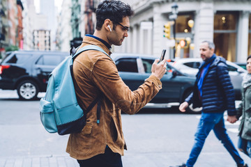 Hispanic young man walking down street and messaging on cellphone