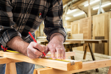 Close-up. Carpenter with pencil and the meter marks the measurement on a wooden board. Construction industry, carpentry workshop.