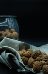 nuts on kitchen cloth, in the back a jar full of nuts, on a black background, healthy food concept.