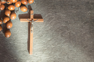 Old wooden Franciscan rosary, on the large Christian cross Jesus, a ray of sunshine illuminates the rosary on a gray stone background, religious and faith concept.