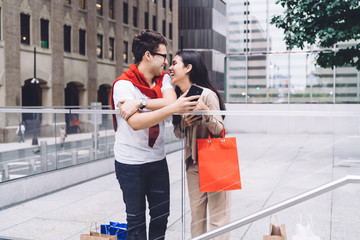 Fototapeta na wymiar Stylish excited multiethnic couple using smartphones on street