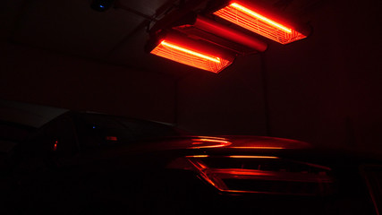 In the dark, detail of the car body is drying under the lamps after painting. red lamps for drying painted parts are switched on in the service station.