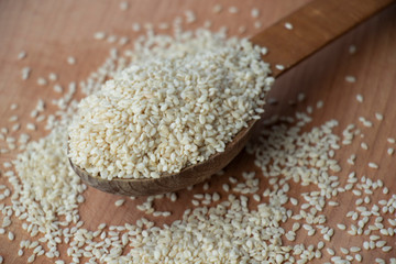 Full spoon of white sesame seed on a wooden board. Wooden spoon on a white background. Home.