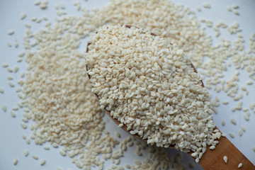 Full spoon of white sesame seed on a wooden board. Wooden spoon on a white background. Home.