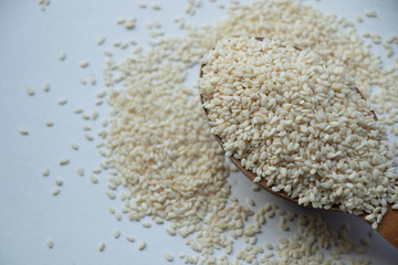 Full spoon of white sesame seed on a wooden board. Wooden spoon on a white background. Home.