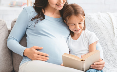 Happy girl having fun while reading book with pregnant mom