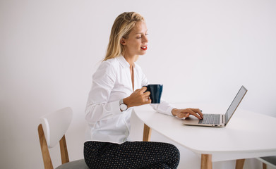 Young blonde with cup sitting and working at laptop