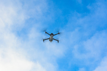 Small gray drone flying in the sky, quadcopter on a cloudy sky background.
