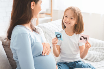 Girl holding pink and blue cards next to mom belly