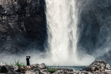 Large rushing waterfall with person at base taking photos, horizontal.