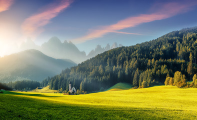 Naklejka premium Wonderful Sunny Landscape of Dolomite Alps. St Johann Church, Santa Maddalena, Val Di Funes, Dolomites, Italy. Fairy velley in Dolomites mountains under sunlit. Amazing nature Background. Epic Scenery