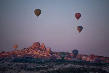 Fototapeta na wymiar Cappadocia, Turkey: aerial view of Uchisar, ancient town of the historical region in Central Anatolia rich of exceptional natural wonders, with hot air balloons floating in the pink sky at dawn 
