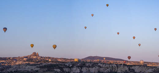 Cappadocia, Turkey: aerial view of Uchisar, ancient town of the historical region in Central Anatolia rich of exceptional natural wonders, with hot air balloons floating in the pink sky at dawn 