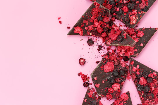 Broken black chocolate bar pieces with scattered dried red berries on pink