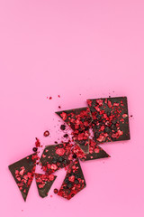 Broken dark chocolate bar pieces with scattered dried red berries on pink