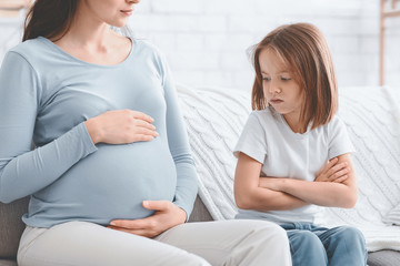 Upset little girl looking at her pregnant mother belly