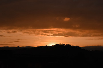 Beautiful orange sunset, the sun is hidden behind the mountains and trees