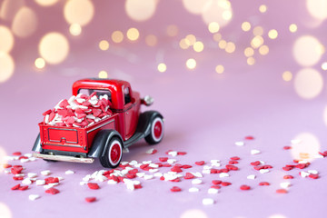 Toy red car with a gift box on the roof on a pink background. Valentines Day background.