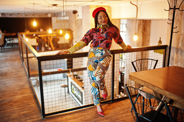 Enthusiastic african american woman in trendy coloured outfit with red beret chilling in cozy cafe.