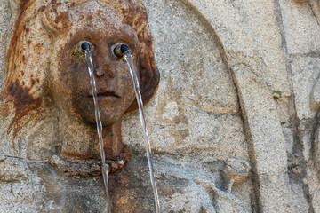 Fragment of a fountain in the form of a child's face with water jets from the eyes. Selective focus.
