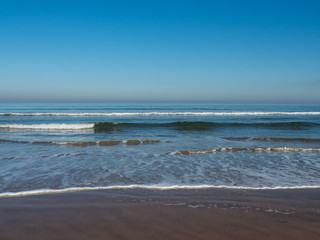 Gentle waves rolling into the beach on a sunny day, with a perfect blue sky and view of the  hazy horizon. Saltburn-by-the-Sea, North Yorkshire - UK