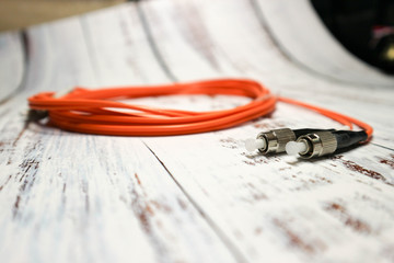 Orange optical fiber network cable with black connectors isolated on wooden background