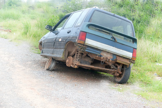 The car is on the side of the road without a left rear wheel