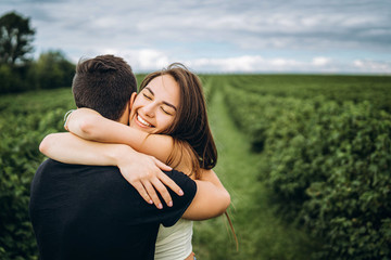 Cute young girl with long hair hugs her lover, smiling and with her eyes closed. Young couple walking in a field in nature