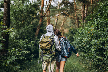 Back view of young couple with backpacks on their backs in the forest. Loving man hugging his...