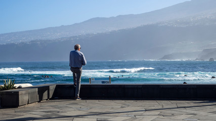 un hombre mayor mirando el mar con la montaña al fondo