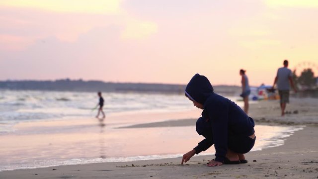 Boy writes words on sand. Little boy writing on the beach sand