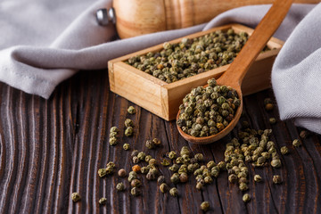 green peppercorns in wooden scoop on rustic background