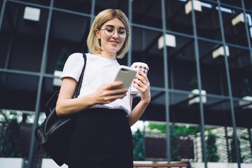 Woman in formal clothes and in glasses using smartphone on street