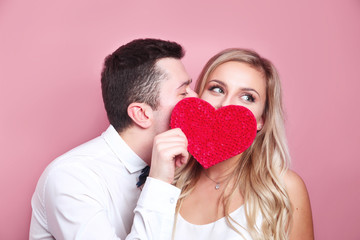 Young couple holding red love heart over eyes and kissing