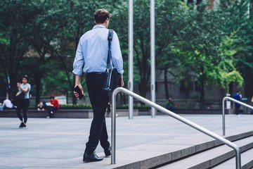 Confident employee holding leather bag and smartphone walking on street