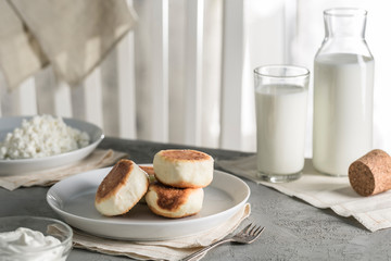 Cheesecakes from cottage cheese on a plate with sour cream and a glass of milk.
