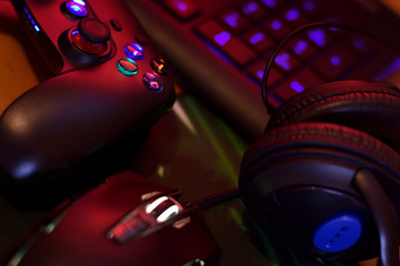 Modern gamepad and gaming mouse lies with keyboard and headphones on table in dark playroom scene....
