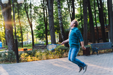 Fototapeta premium A man in jeans and a warm sweater playing a badminton with a racket in his hand give a pass. A shuttlecock flies in the air