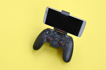 Modern black gamepad for smartphone on yellow background. Mobile video gaming device