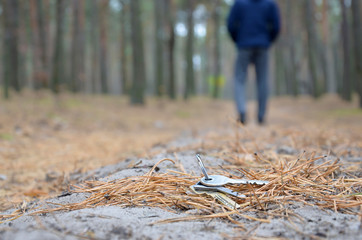 Young man loses his keys bunch on Russian autumn fir wood path. Carelessness and losing keys concept