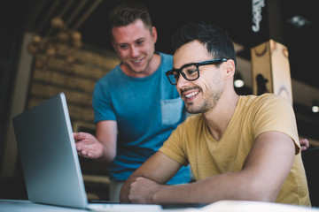 Cheerful young male colleagues working on business project in cafe