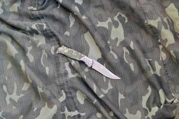 Military knife on army camouflage clothes close up. Background with copy space for military or...