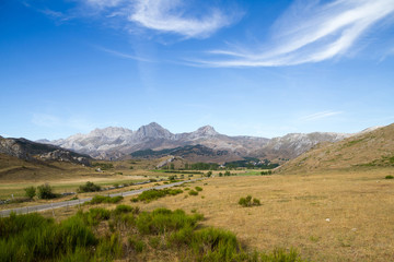 Fototapeta na wymiar Vista de paisaje veraniego con carretera de acceso al pueblo de San Emiliano en un valle rodeado con altas montañas. León. España