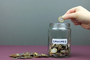 A hand adding money to a savings jar.