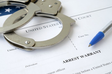 District Court Arrest Warrant court papers with handcuffs and blue pen on United States flag....